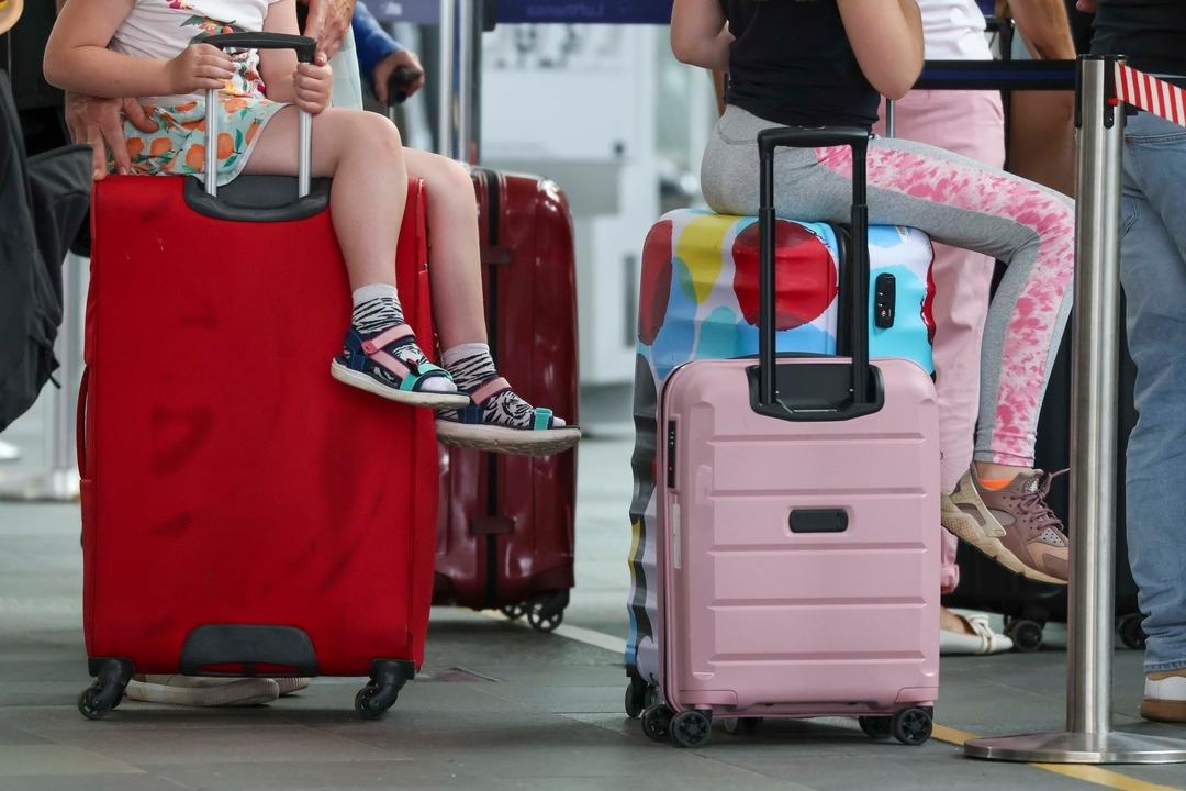 Kinder sitzen am Flughafen auf ihren Reisekoffern 