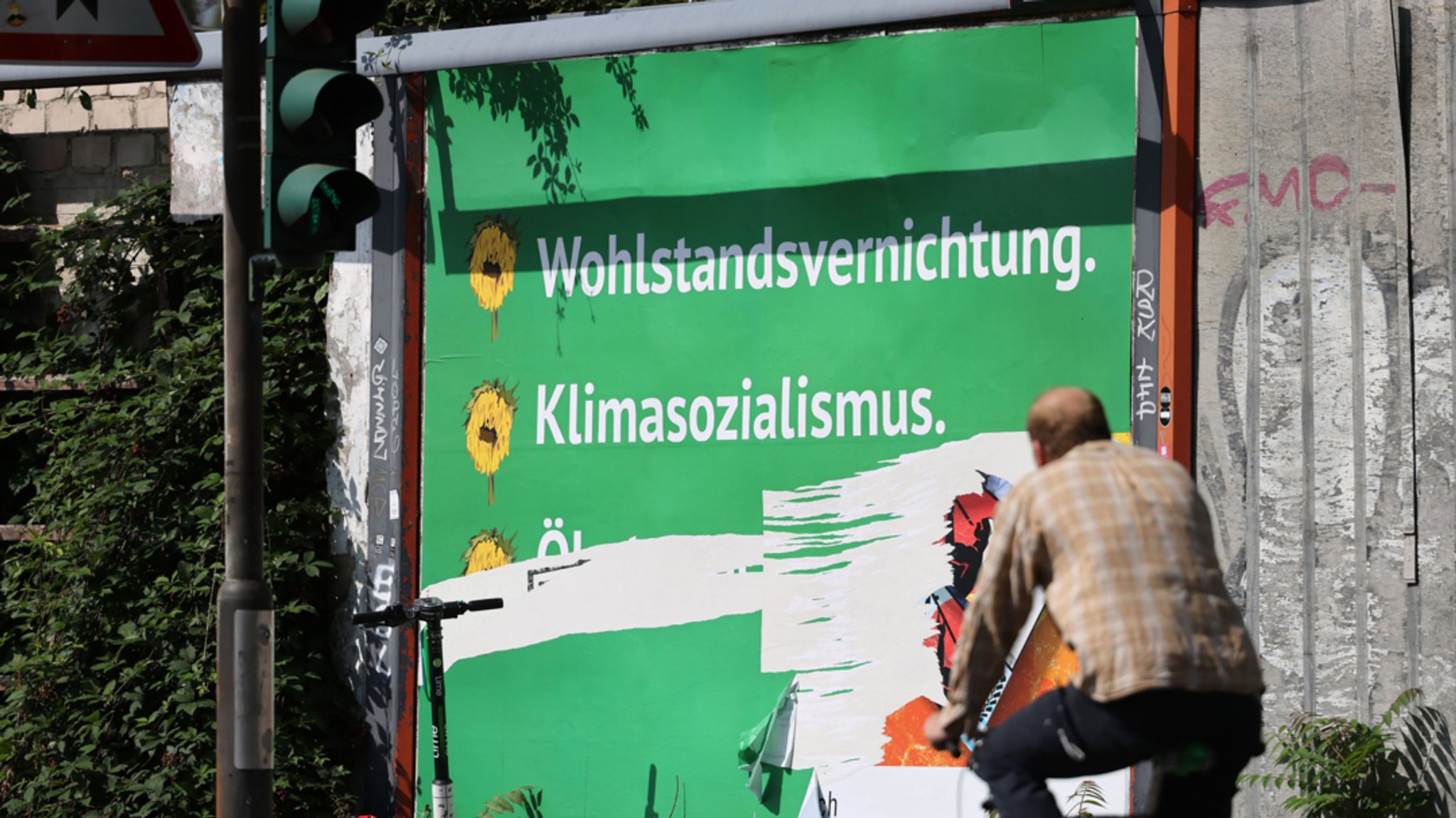 Köln: Ein beschädigtes Plakat mit den Schriftzügen "Wohlstandsvernichtung" und "Klimasozialismus" hängt am Straßenrand. 