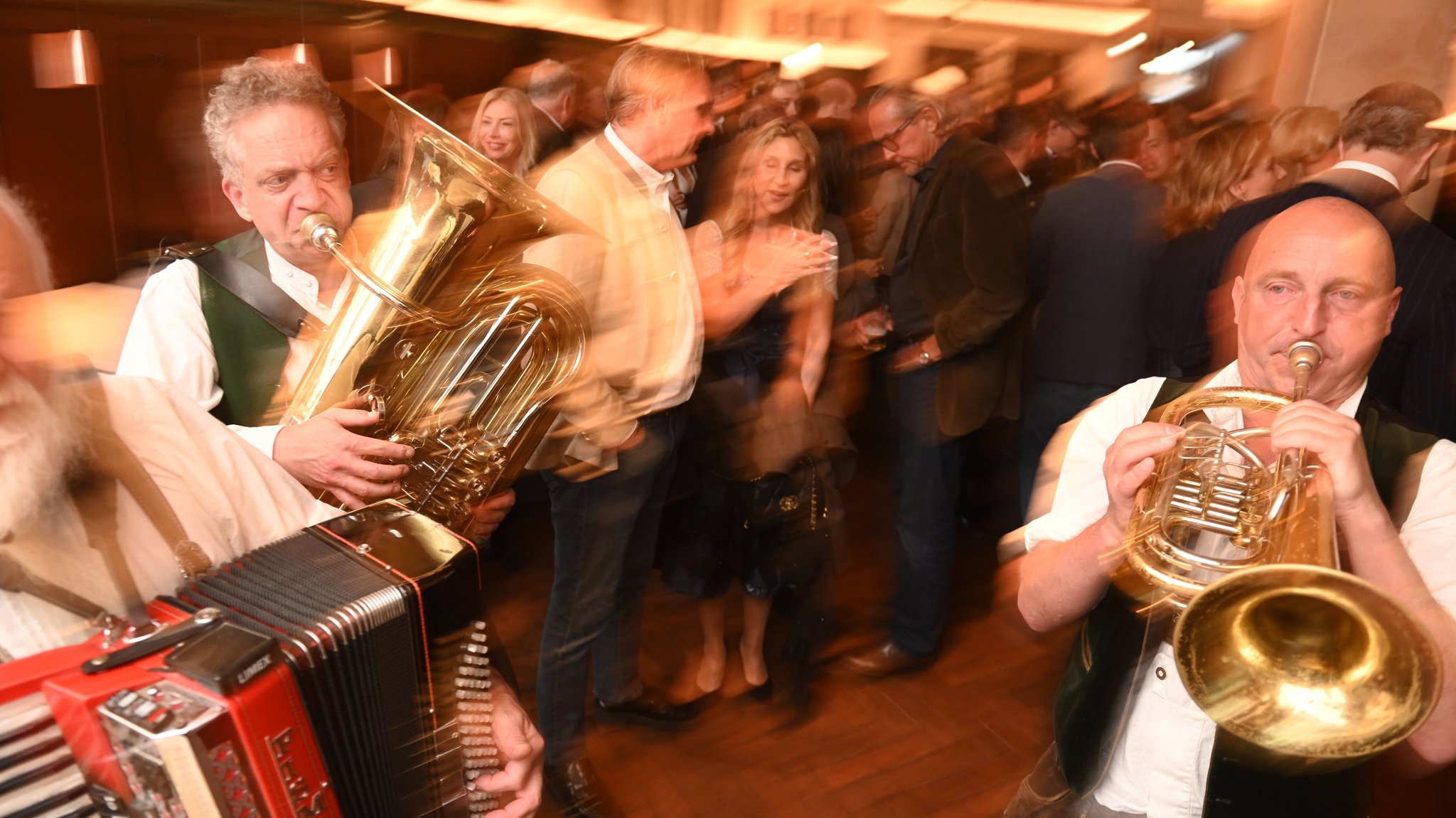 Musikanten spielen bei der Eröffnung eines Wirtshauses in München. Zu sehen sind Blechbläser und ein Akkordeon. Im Hintergrund steht das Publikum.