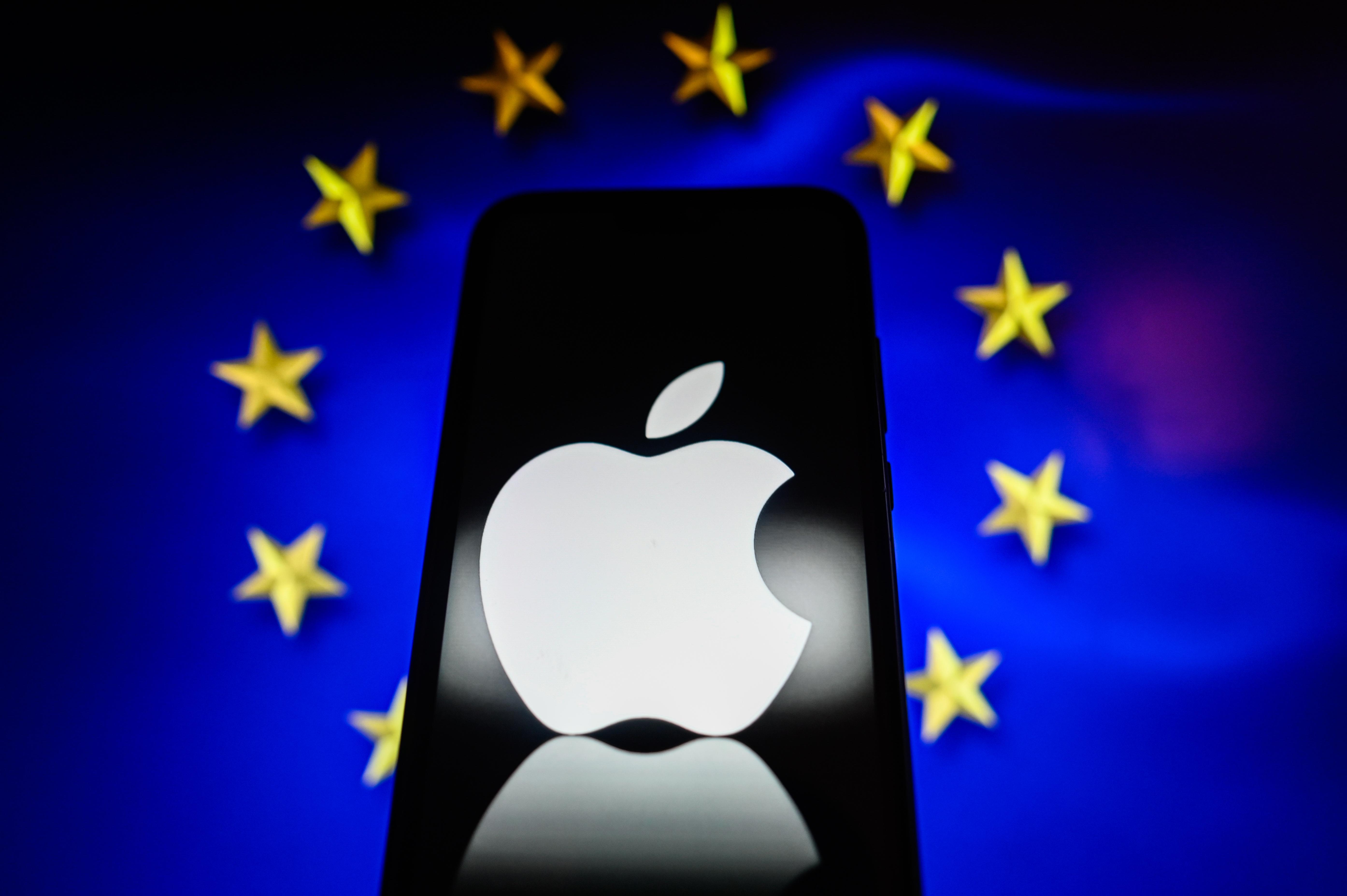 Das Apple-Logo auf einem Smartphone, im Hintergrund die Flagge der EU