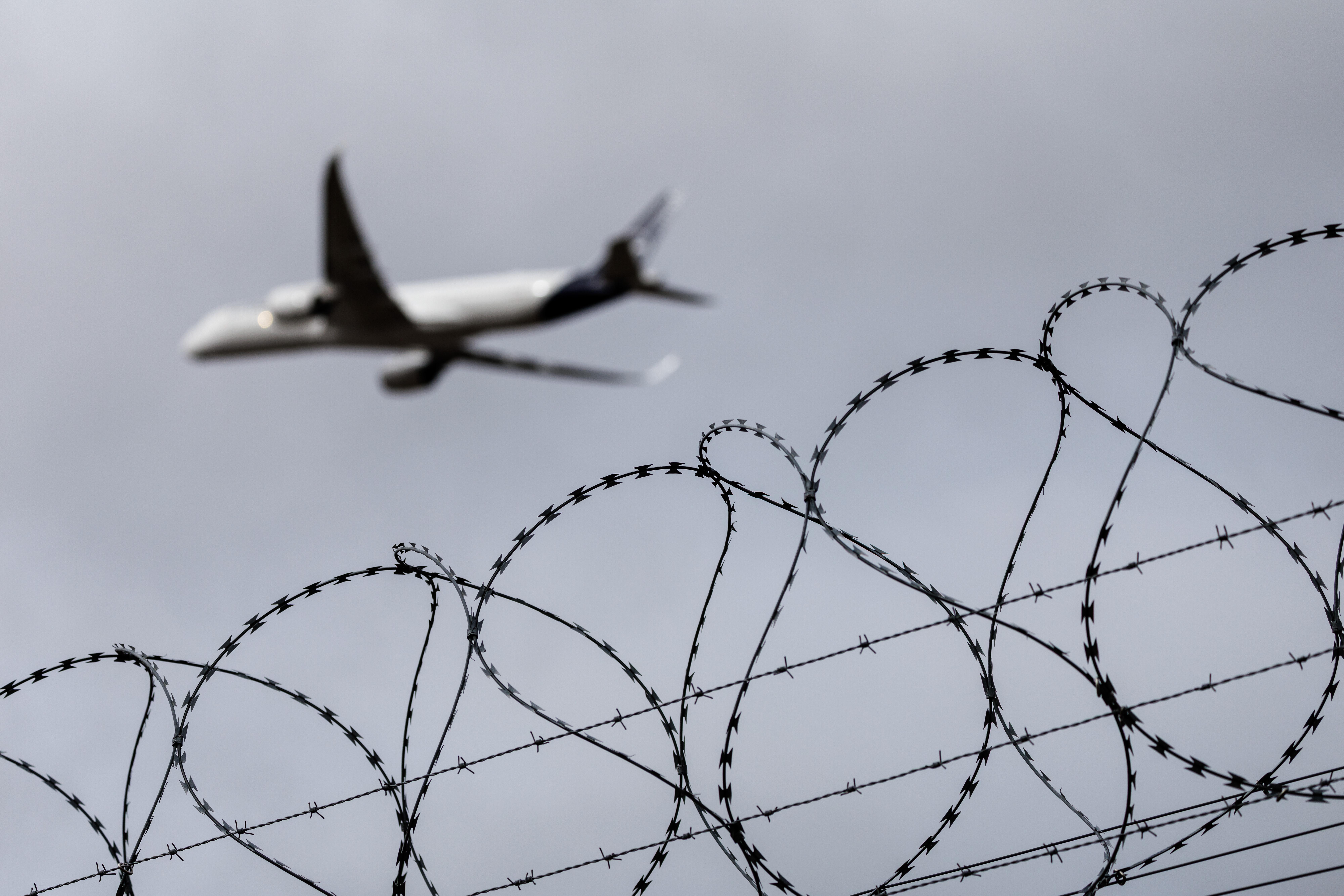 Ein Stacheldraht ist am Flughafengelände in München (Bayern) zu sehen, während im Hintergrund ein Flugzeug startet.
