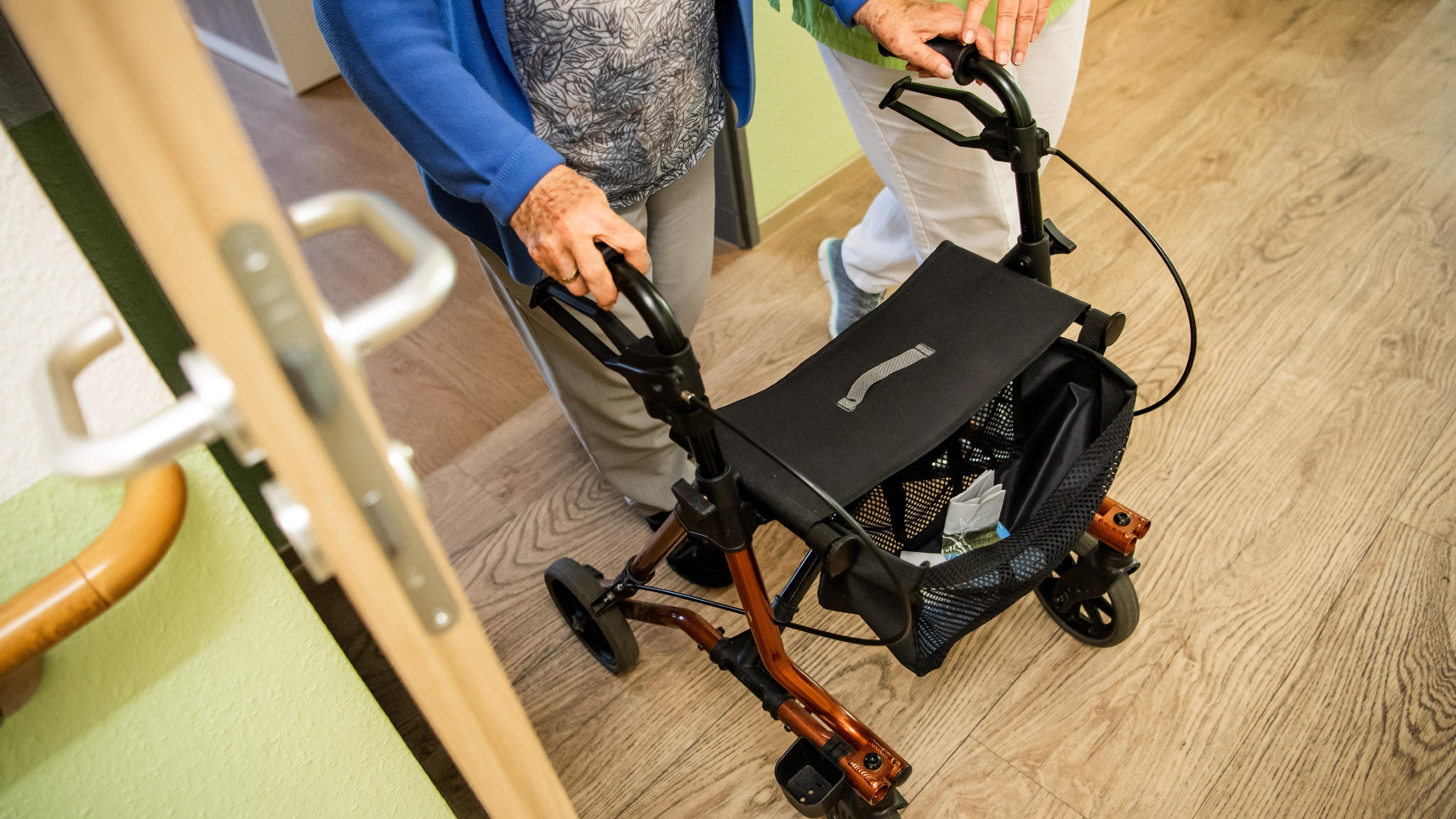 Eine ältere Dame läuft an einem Rollator, neben ihr eine Pflegekraft