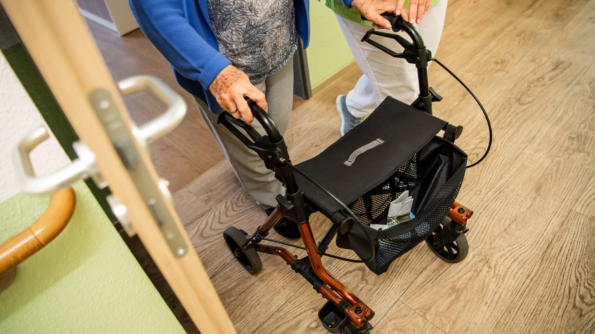 Eine ältere Dame läuft an einem Rollator, neben ihr eine Pflegekraft