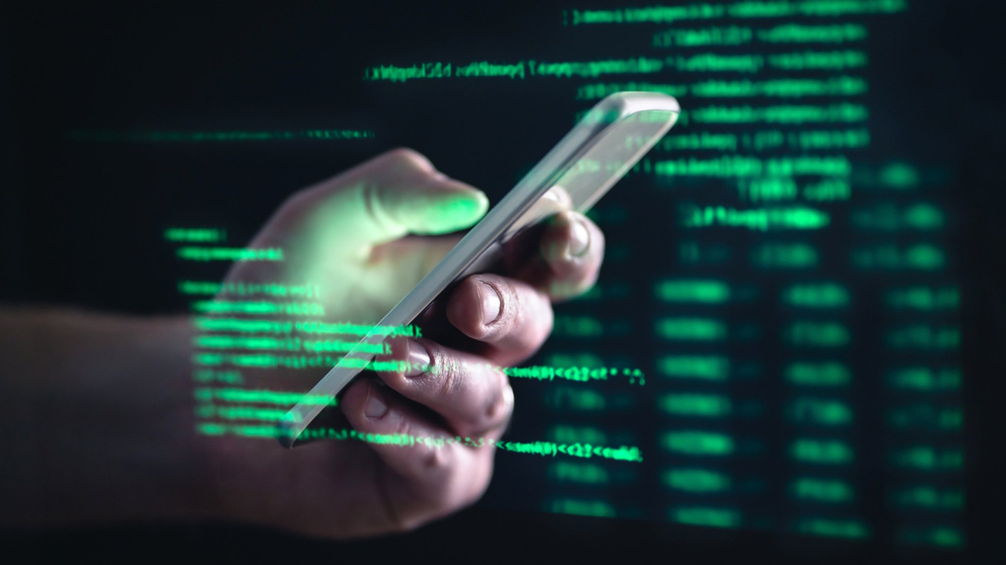 Eine Männerhand mit einem Smartphone in dunkler Umgebung mit leuchtend grünen Computercodes.