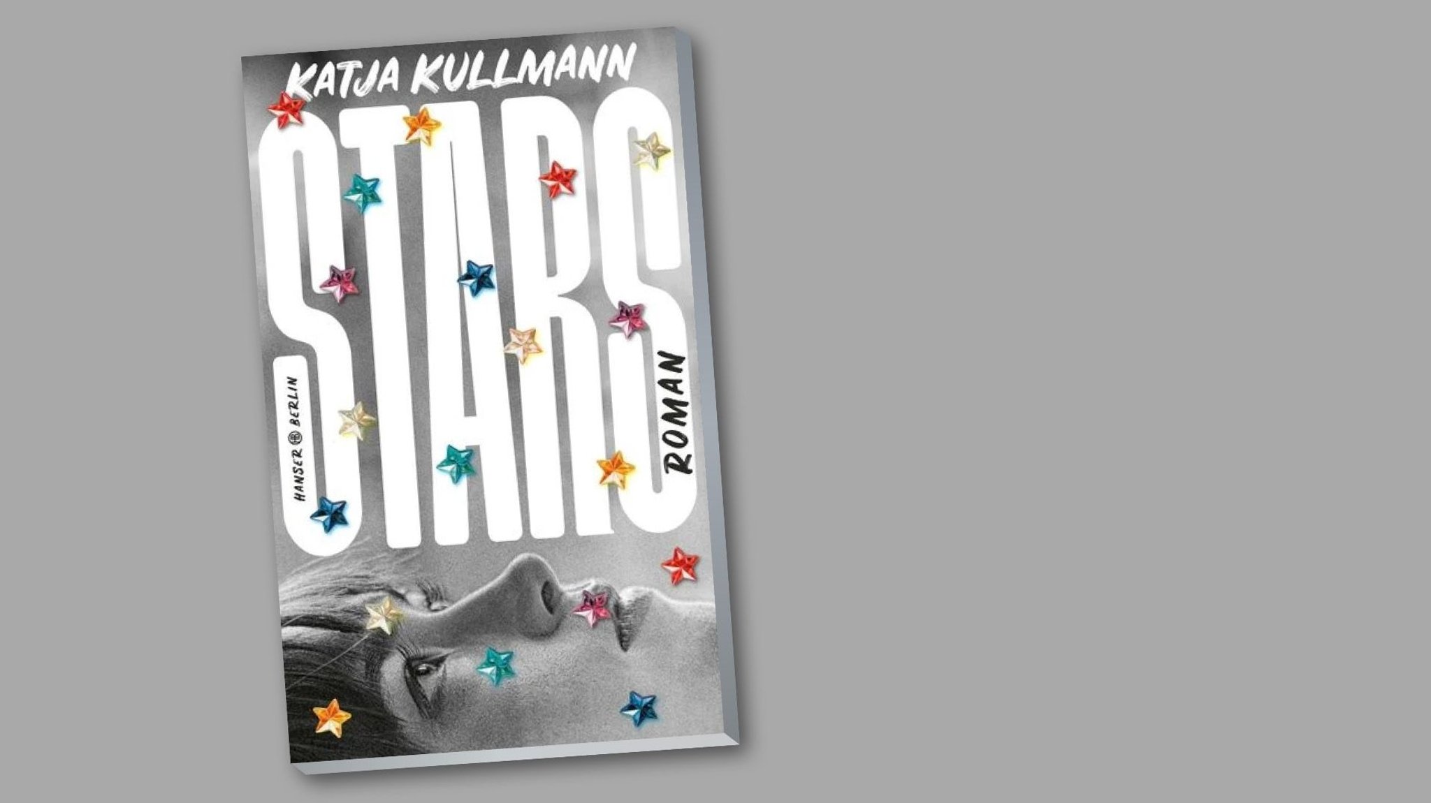 Das Buchcover von Katja Kullmanns Roman "Stars" zeigt ein schwarzweiß fotografiertes, liegendes Frauengesicht, das nach oben schaut. Über das schwarzweiße Cover sind bunte Sterne verteilt.