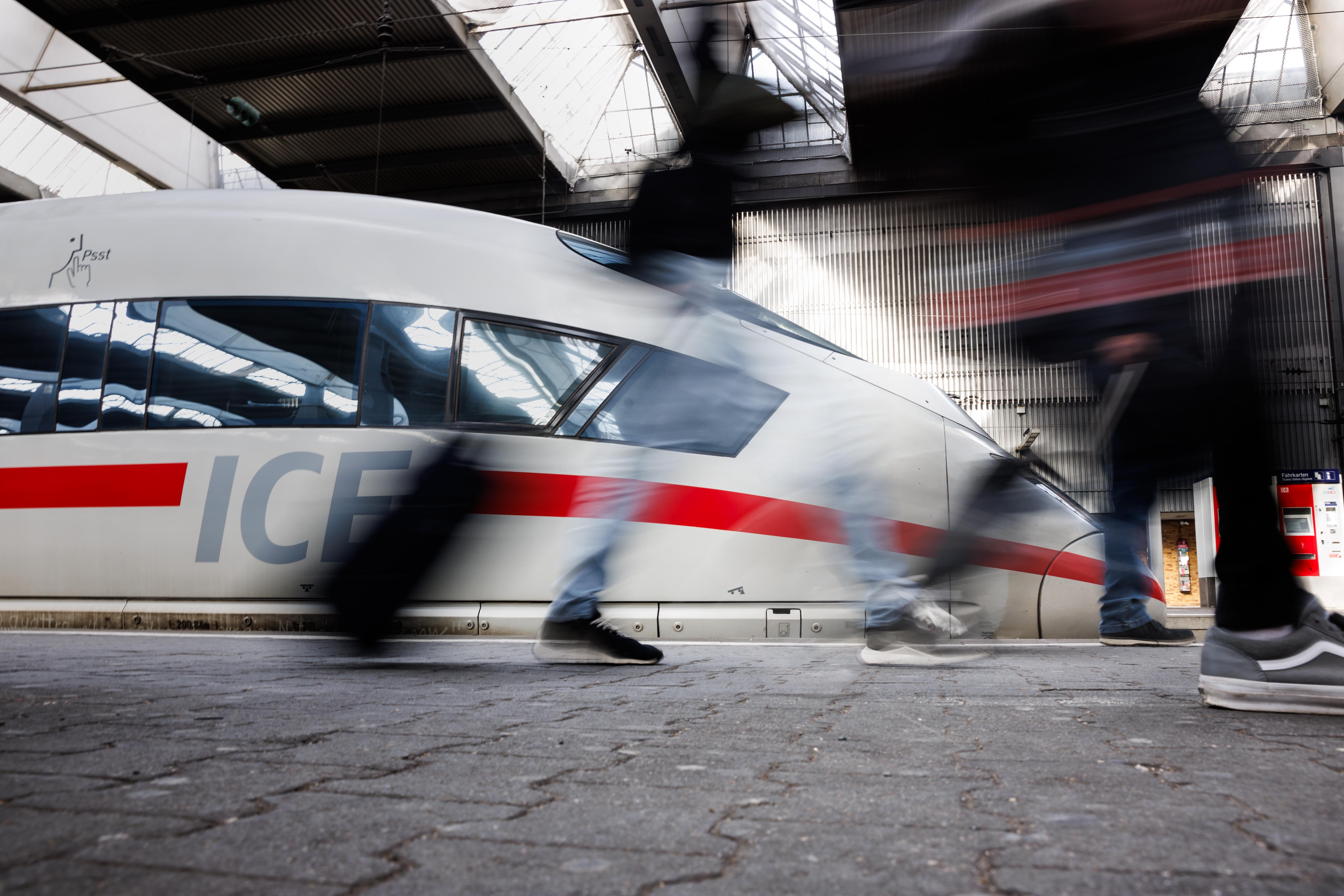 Reisende gehen an einem Bahnsteig an einem ICE der Deutschen Bahn am Hauptbahnhof von München vorüber.