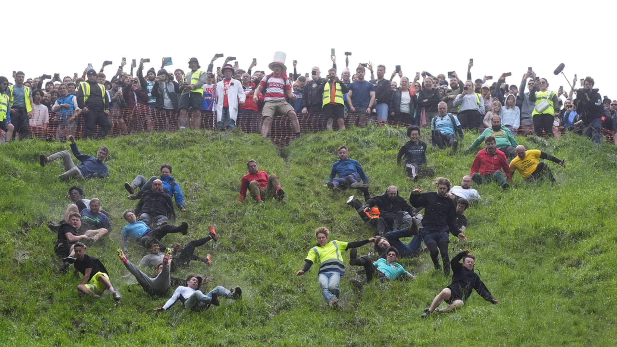 Menschen rollen Grashügel beim Käserennen hinunter 