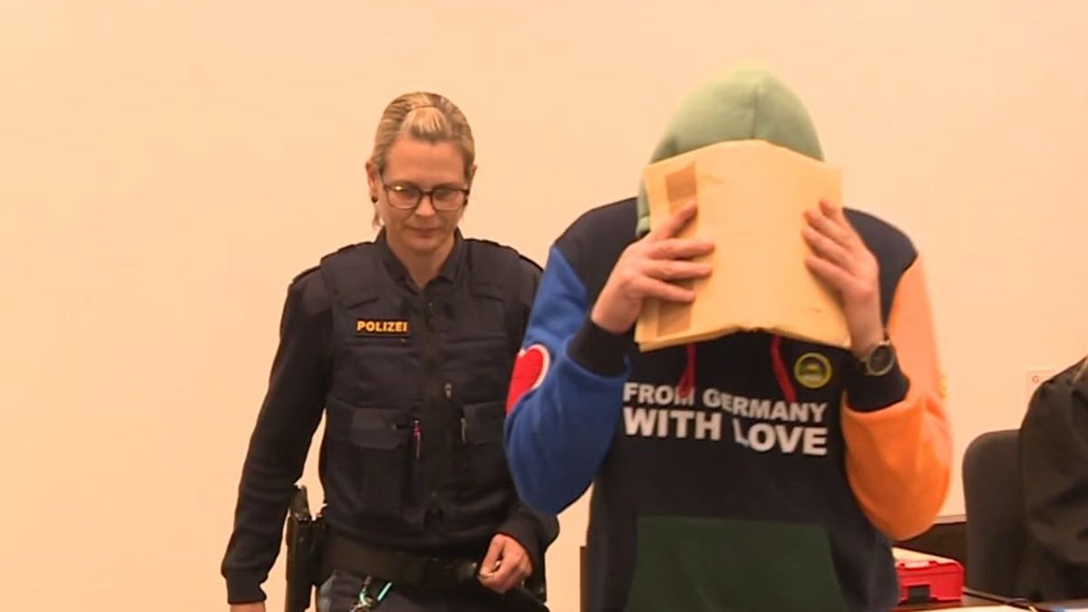 Eine Polizistin begleitet den an den Füßen gefesselten Angeklagten in den Gerichtssaal.