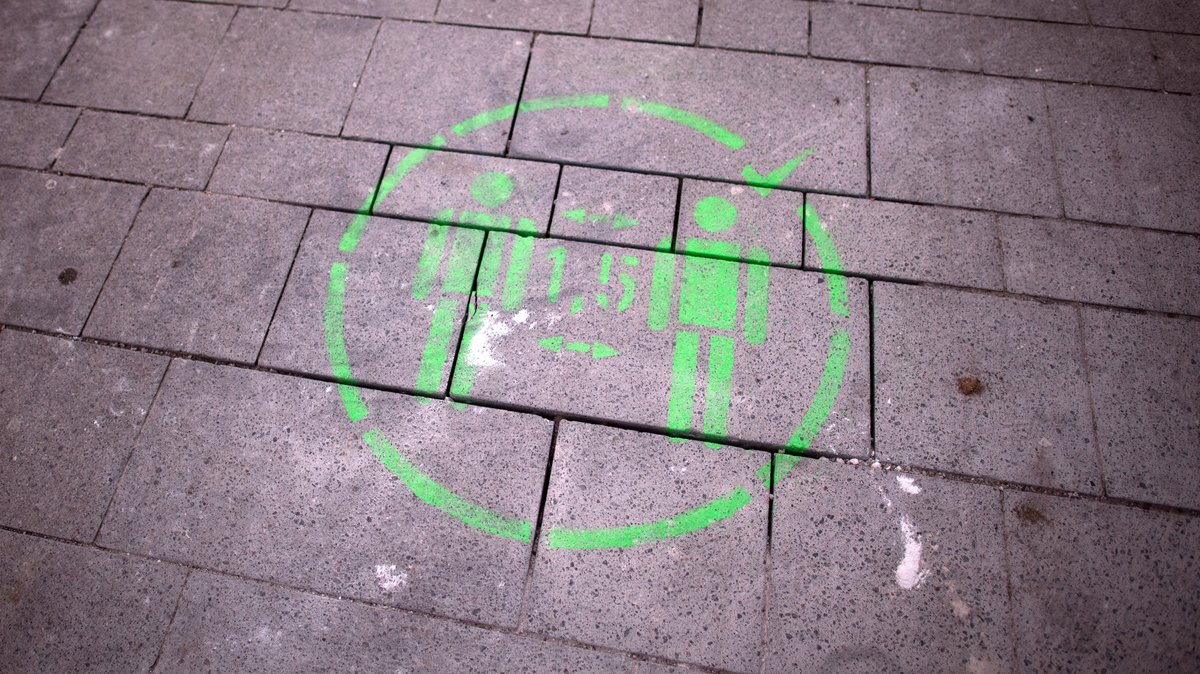Ein Piktogramm mit dem Hinweis zum Abstandhalten ist auf Straßenpflaster gemalt.