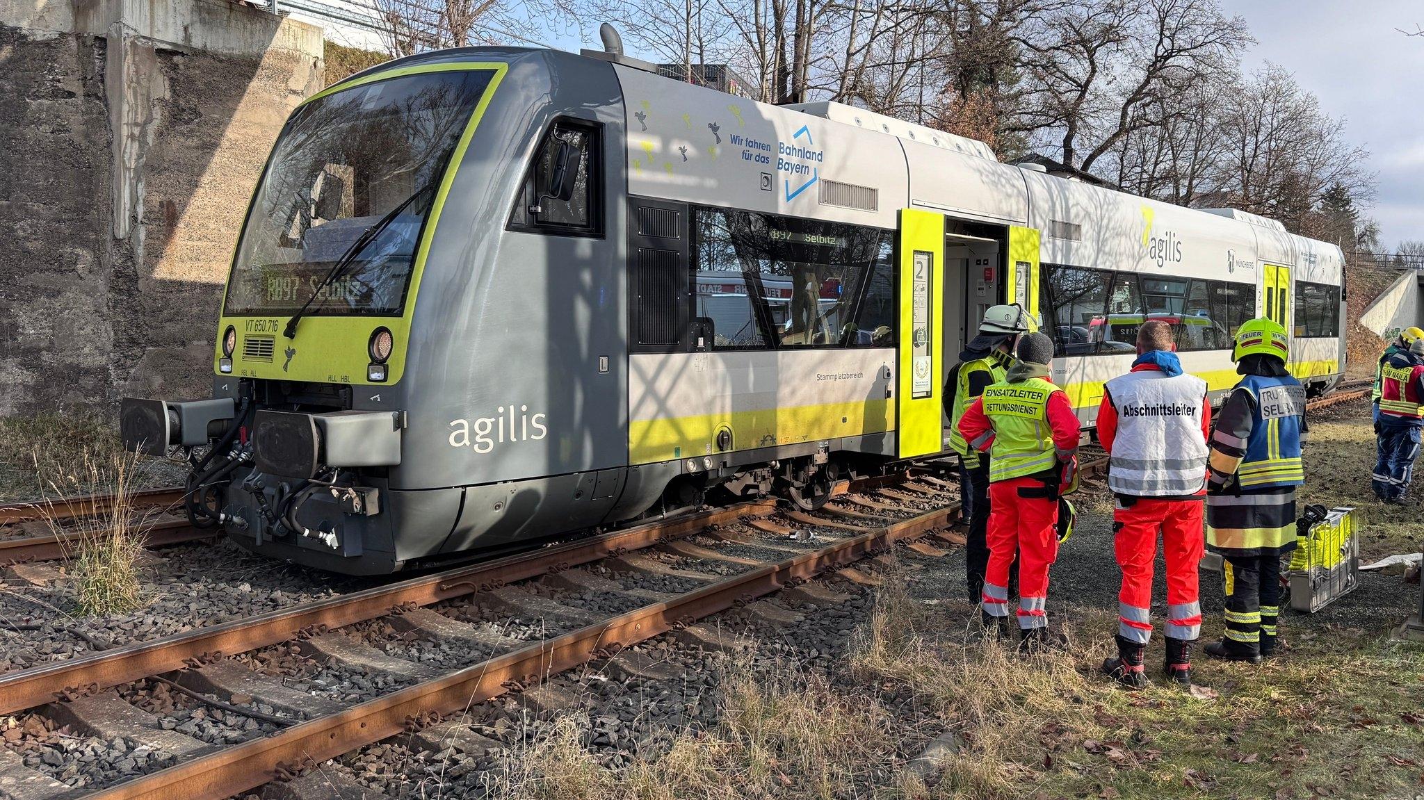 Ein Triebwagen steht neben dem Zuggleis, vier Retter blicken auf den Schaden.