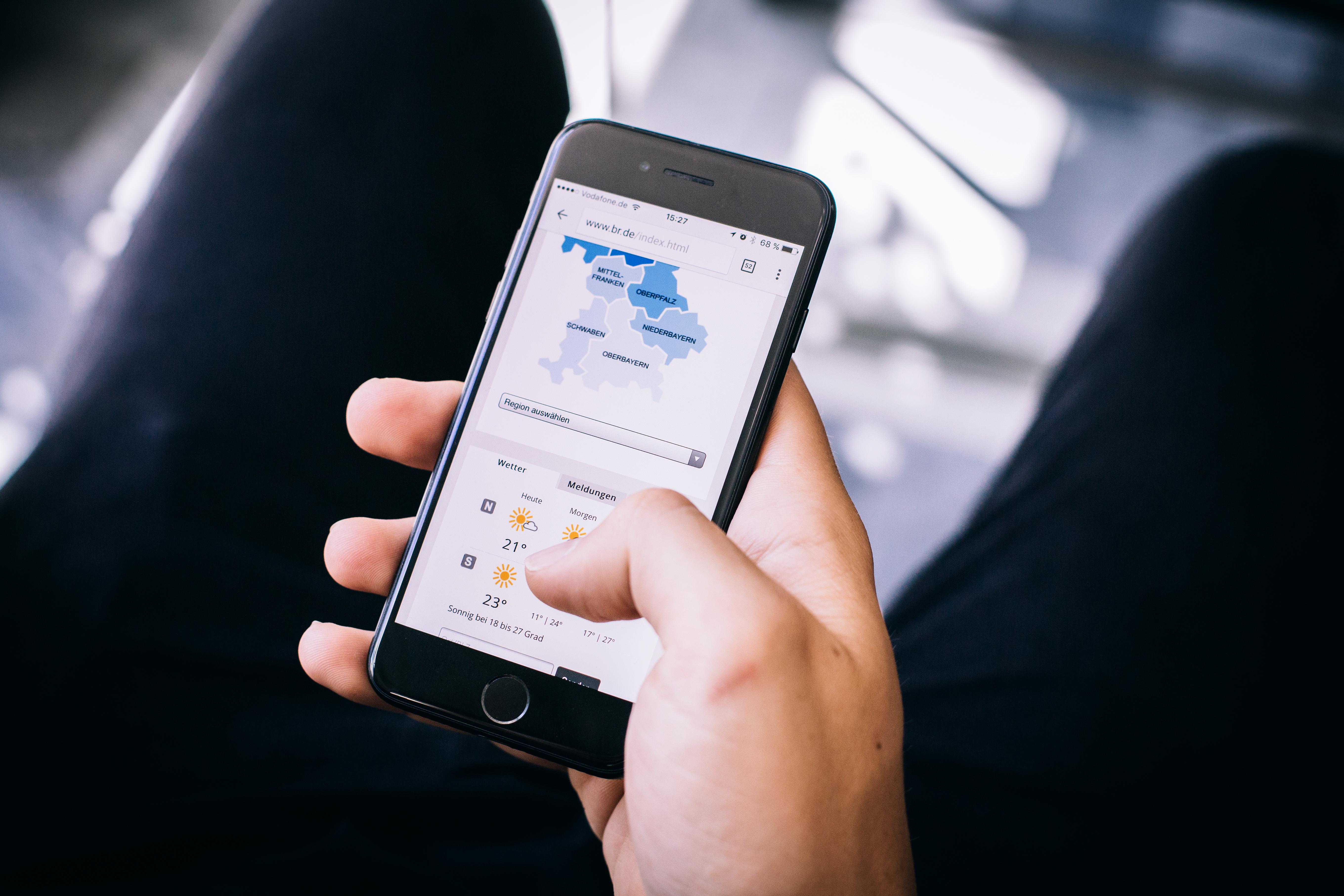 Eine Hand hält ein Handy mit einer Bayernkarte und dem Wetter auf dem Display