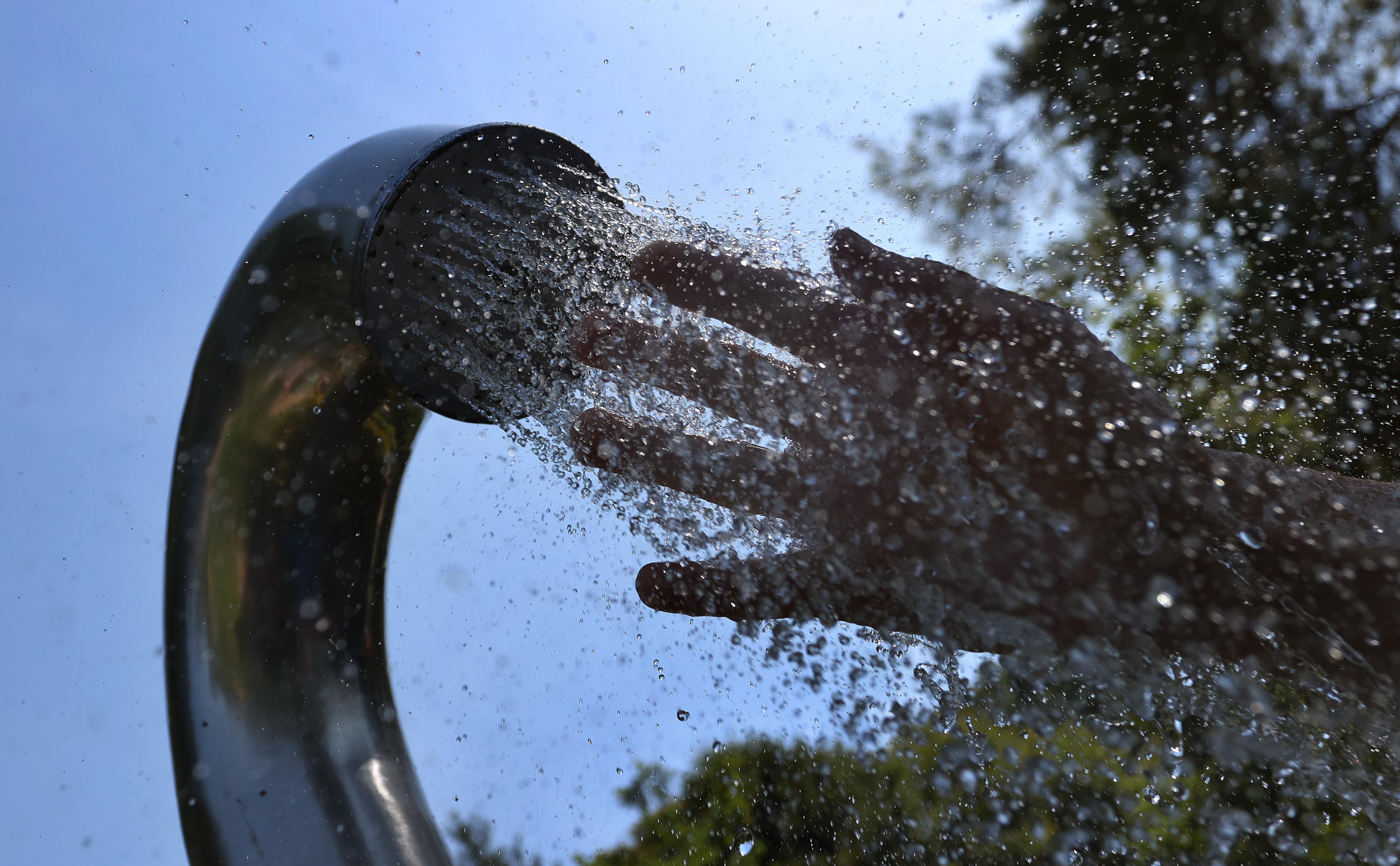 Ein Besucher eines Strandbades kühlt seine Hand unter einer Dusche.