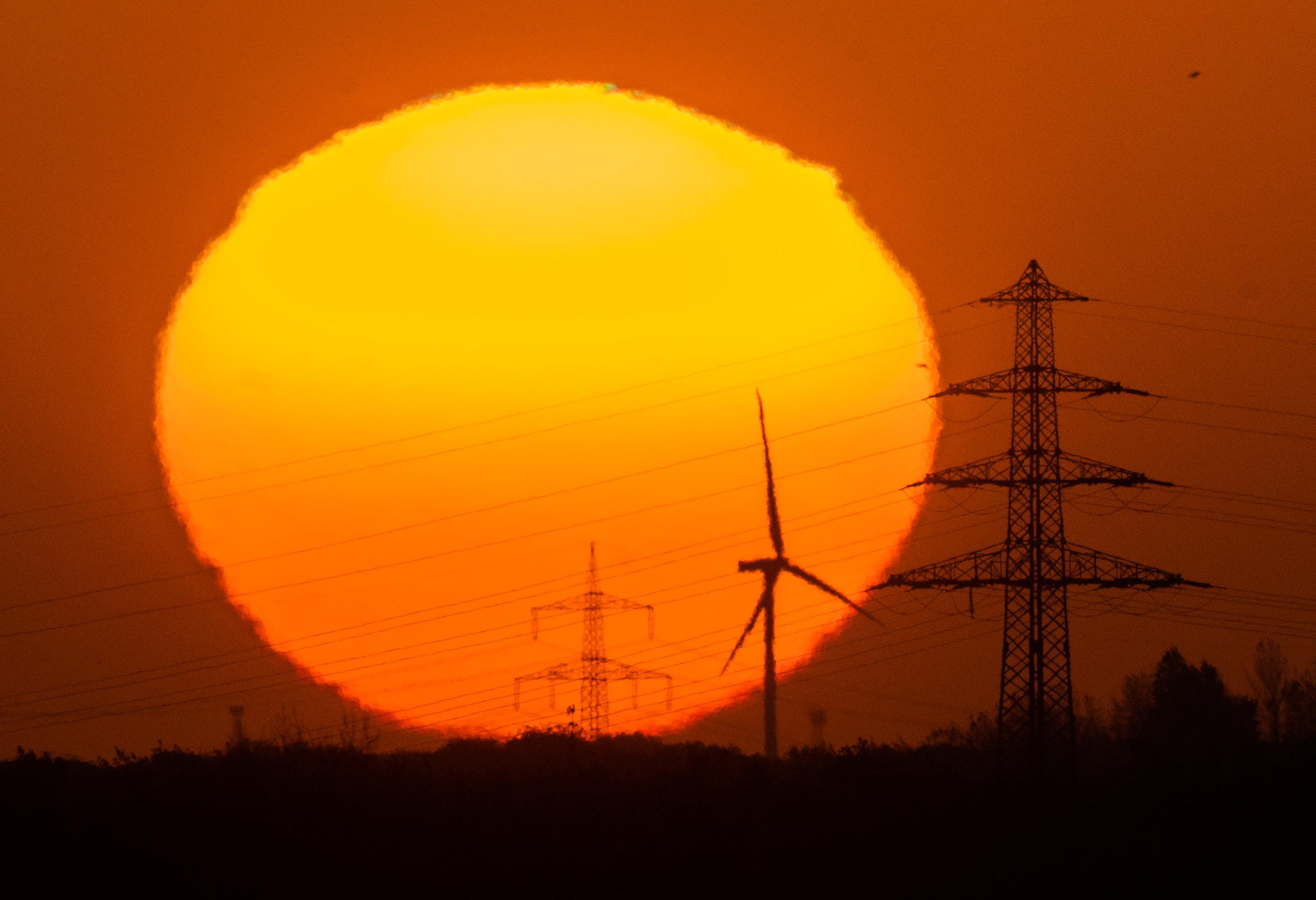 Die Sonne geht hinter Windrädern und Hochspannungsleitungen in der Region Hannover auf.