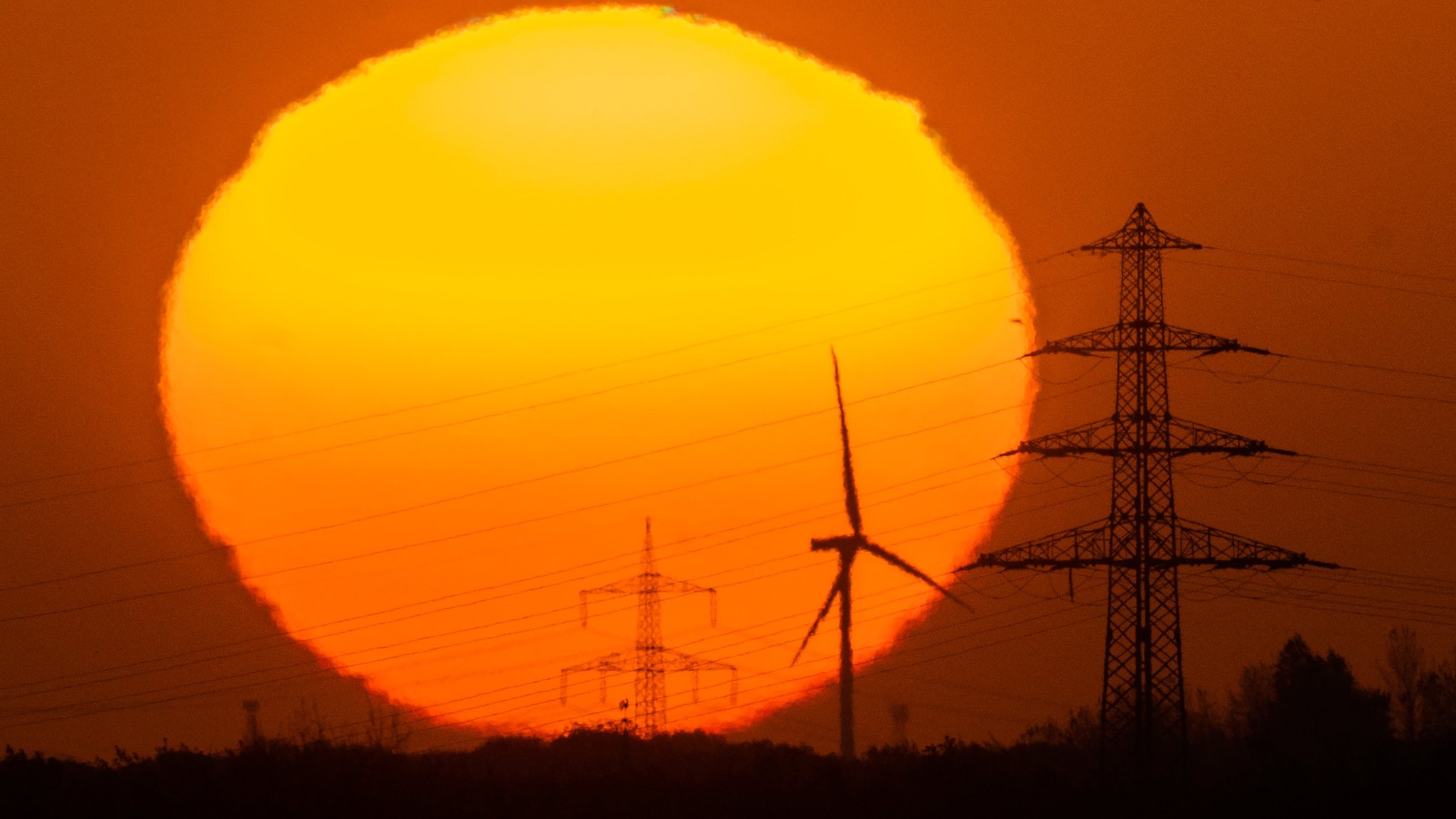 Die Sonne geht hinter Windrädern und Hochspannungsleitungen in der Region Hannover auf.