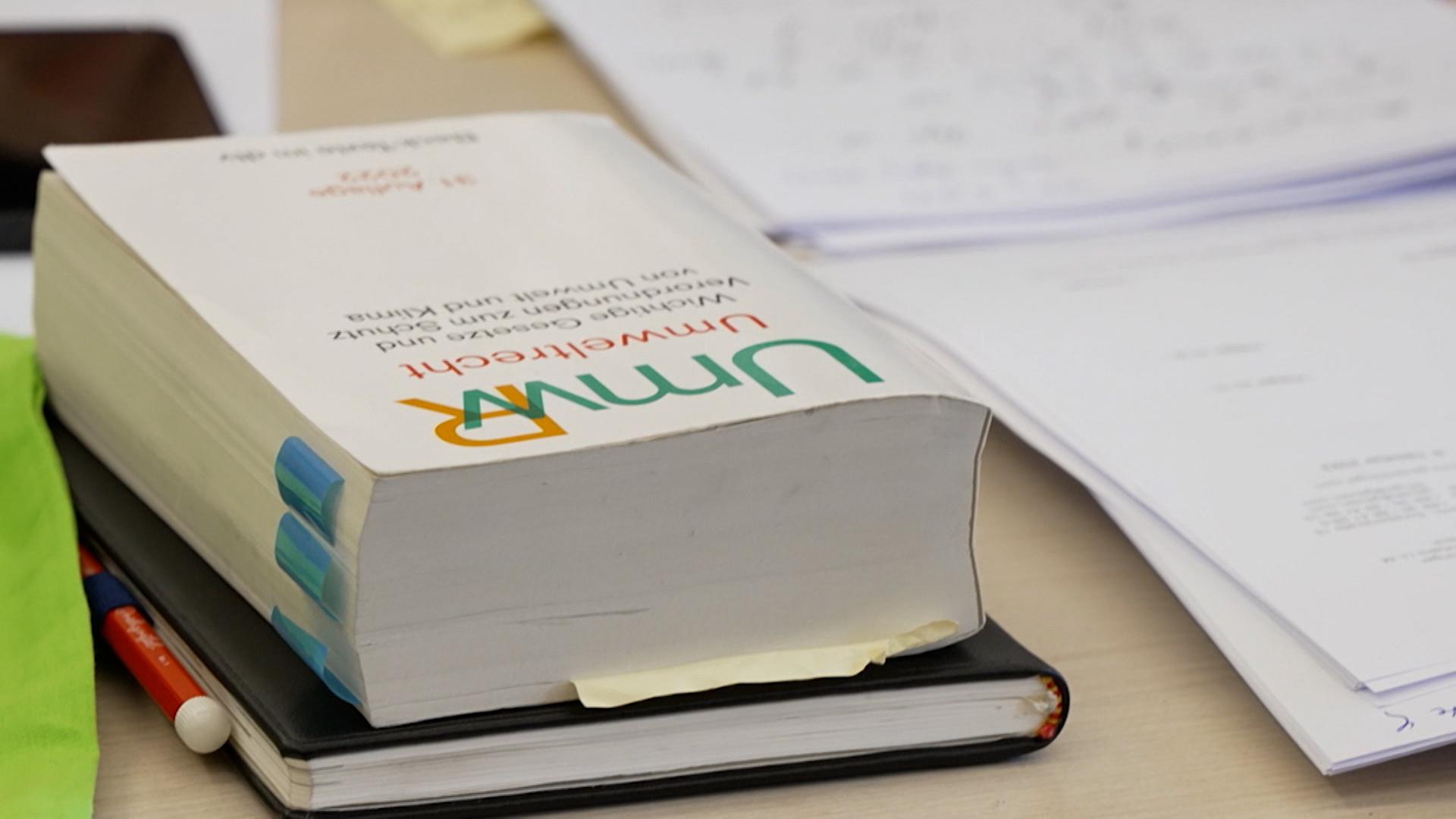Auf einem Tisch liegt ein Buch mit der Aufschrft "Umweltrecht".