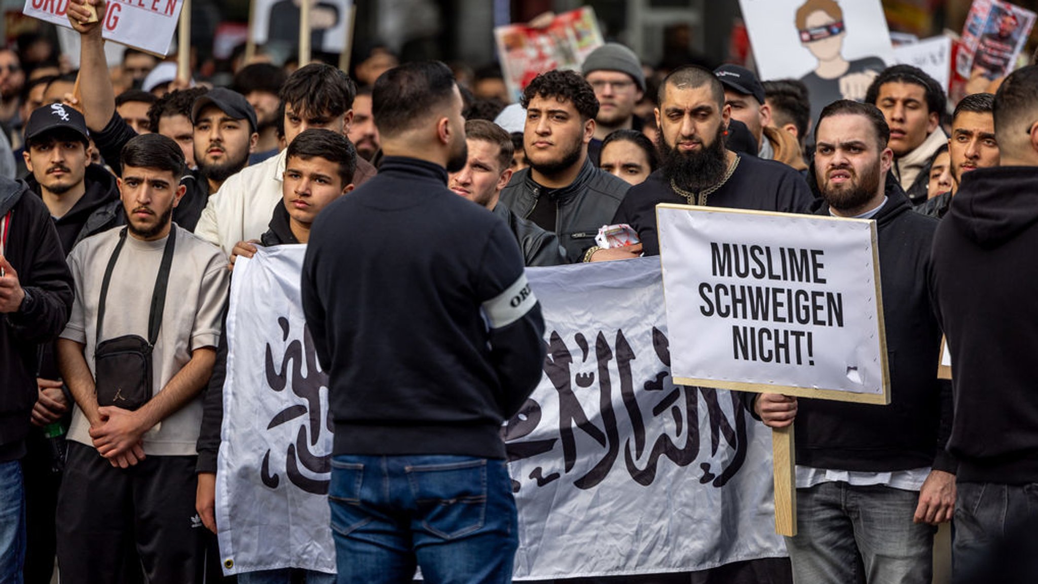 Teilnehmer einer Islamisten-Demo halten ein Plakat mit der Aufschrift "Muslime schweigen nicht" in die Höhe.