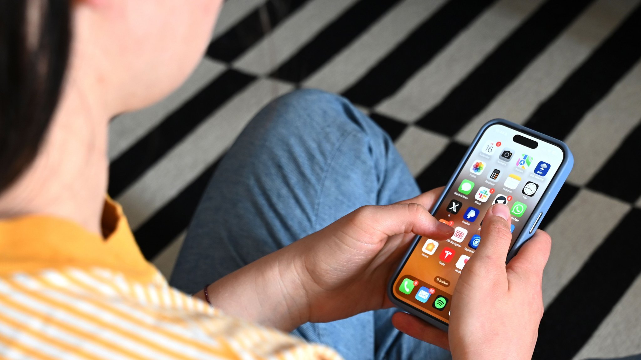 (Symbolbild) Ein junger Mensch schaut auf ein Smartphone