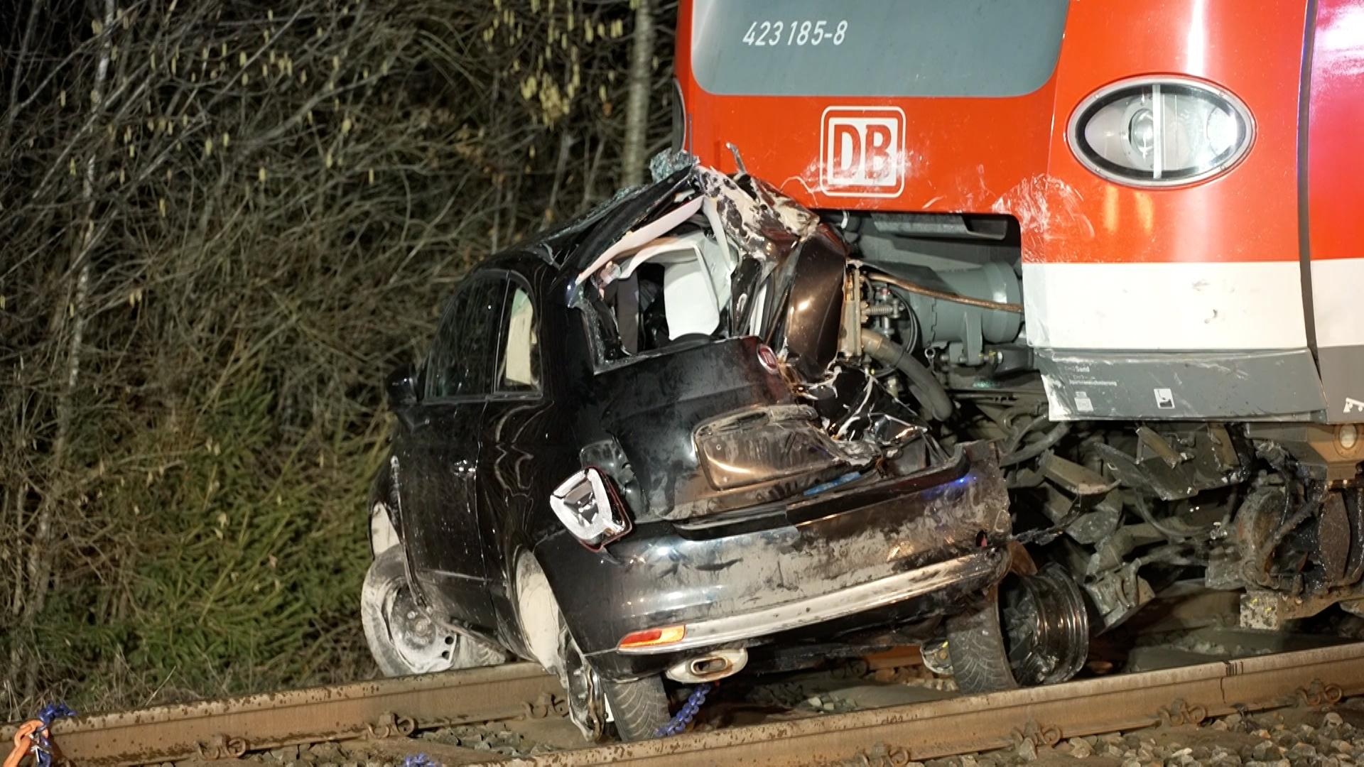 12.02.2026, Bayern, Höhenkirchen-Siegertsbrunn: Ein zerstörter PKW steht nach einem Unfall vor einem S-Bahn-Zug in Höhenkirchen-Siegertsbrunn.