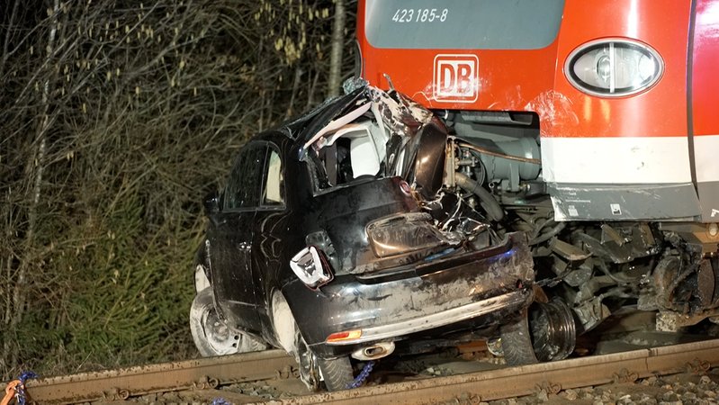 12.02.2026, Bayern, Höhenkirchen-Siegertsbrunn: Ein zerstörter PKW steht nach einem Unfall vor einem S-Bahn-Zug in Höhenkirchen-Siegertsbrunn. | Bild: BR 2026 12.02.2026, Bayern, Höhenkirchen-Siegertsbrunn: Ein zerstörter PKW steht nach einem Unfall vor einem S-Bahn-Zug in Höhenkirchen-Siegertsbrunn.