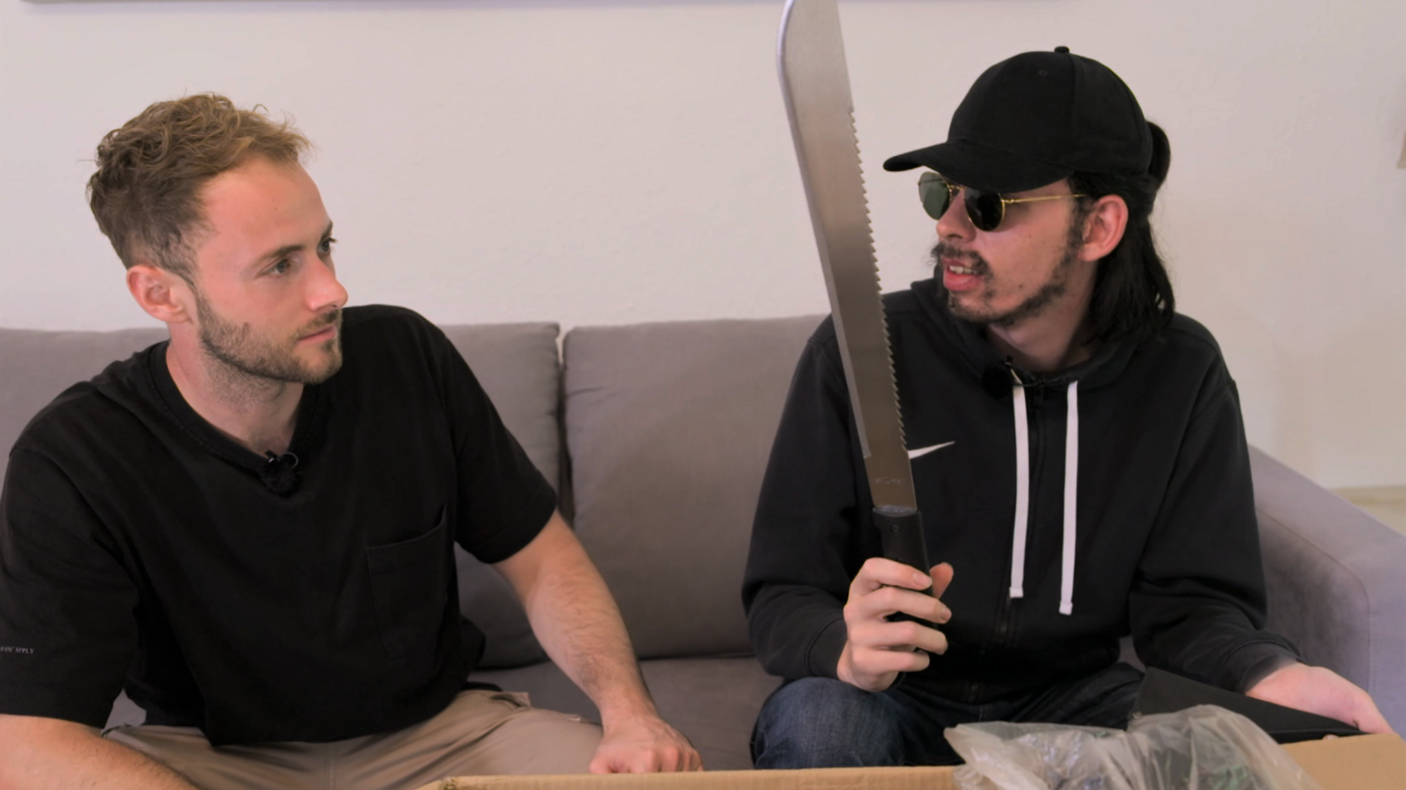 Terror-Aussteiger Dennis (Name geändert) mit Y-Kollektiv-Reporter Tobias Dammers auf der Couch. Er hält eine Machete in der Hand.