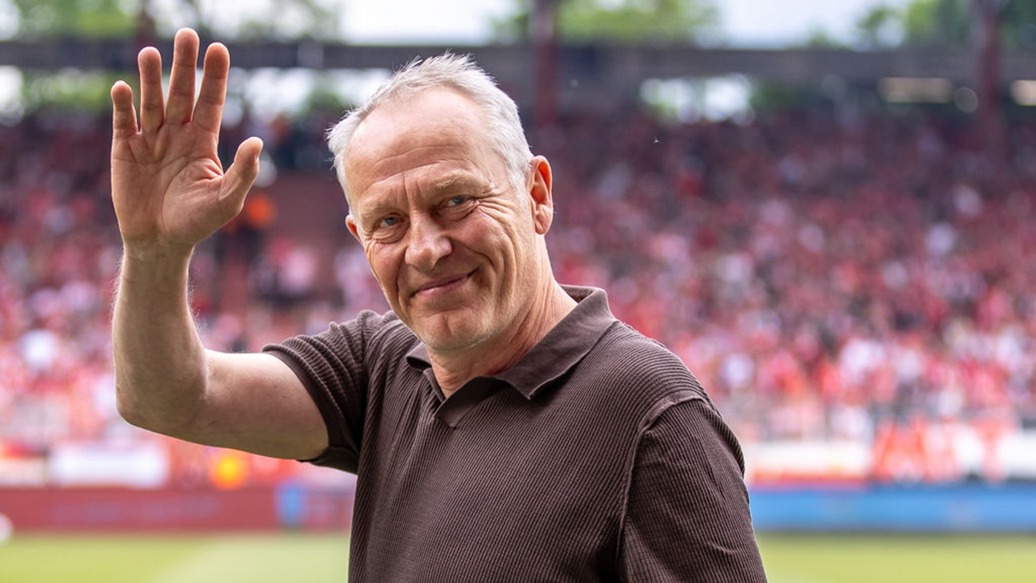 Christian Streich winkt bei einem Fußballspiel in die Kamera