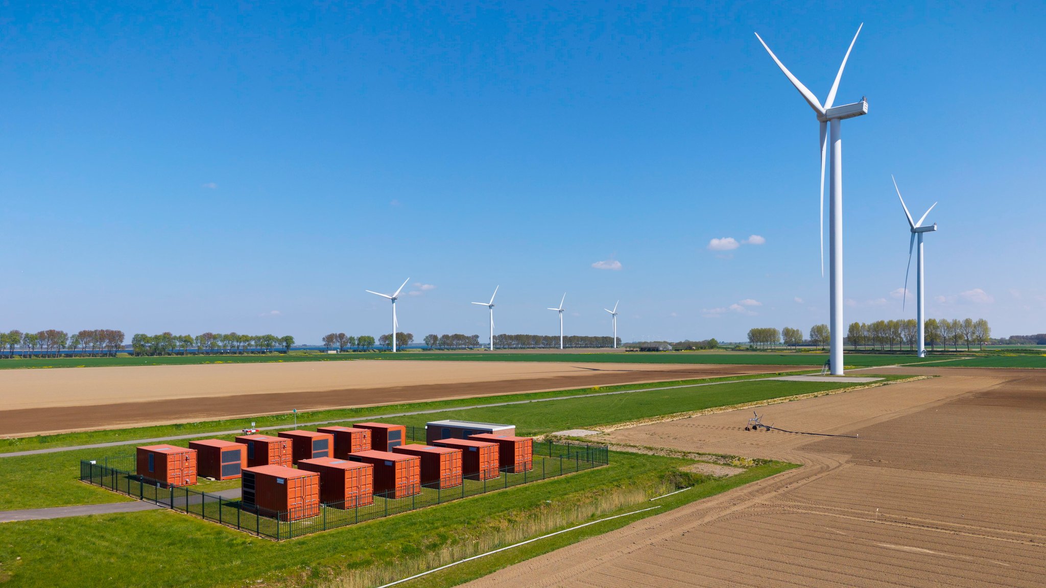 (Symbolbild) Batteriespeicher auf einem Feld, im Hintergrund sind Windräder zu sehen. | Bild: picture alliance / Westend61 / Mischa Keijser (Symbolbild) Batteriespeicher auf einem Feld, im Hintergrund sind Windräder zu sehen.