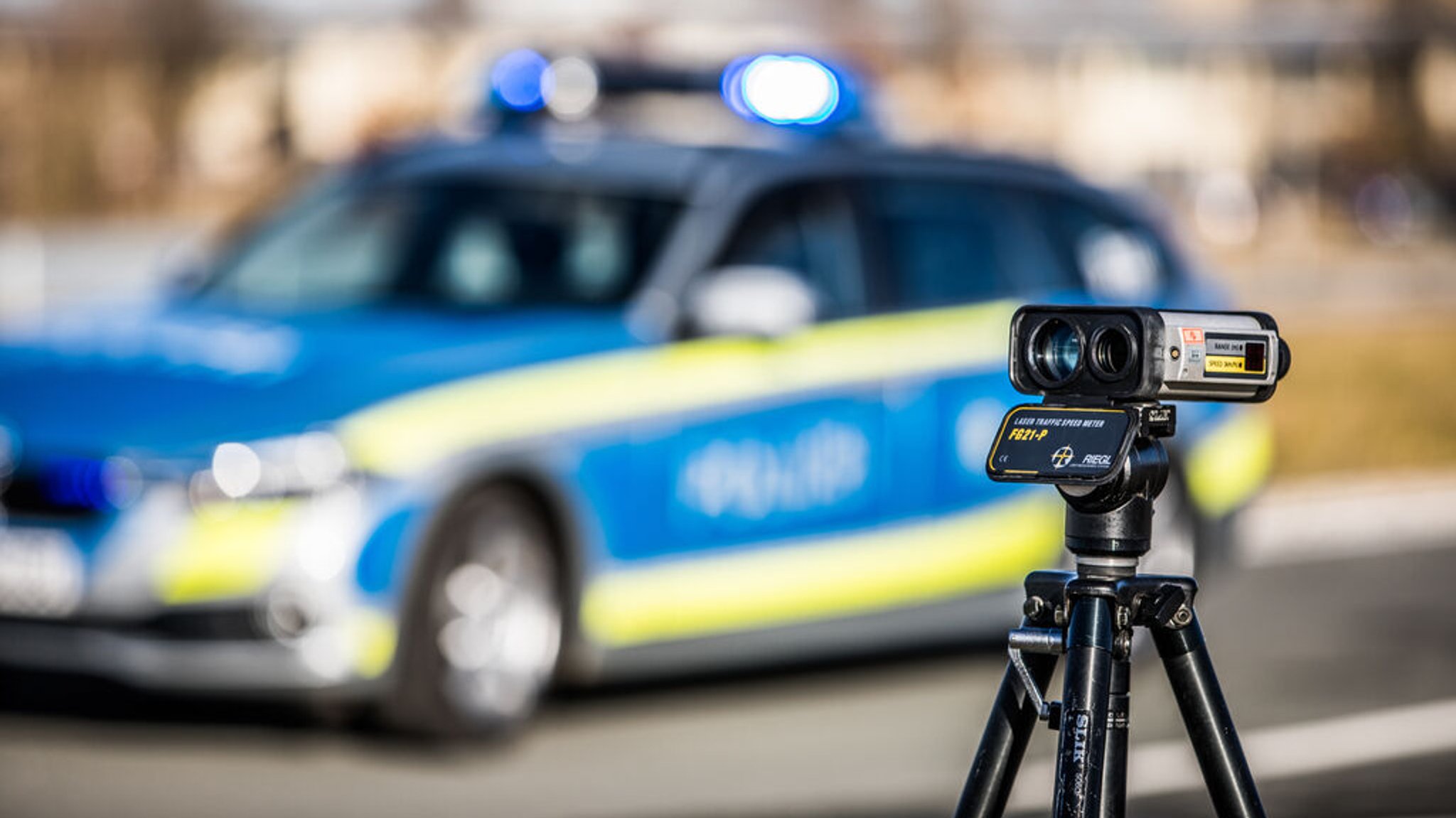 Ein Geschwindigkeitsmessgerät der Polizei steht an einer Straße vor einem Polizeiauto.