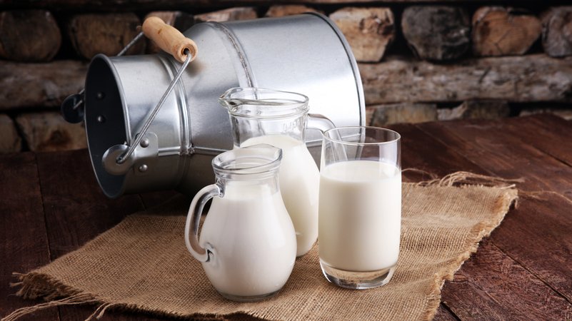 Umgekippte Milchkanne neben in Glaskännchen und Gläser abgefüllter Milch