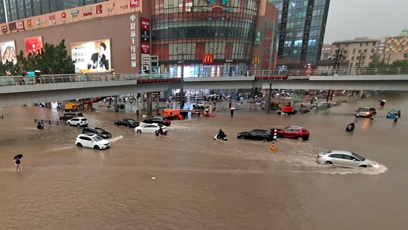 China, Zhengzhou: Fahrzeuge stehen in der zentralchinesischen Provinz Henan auf einer überfluteten Straße.