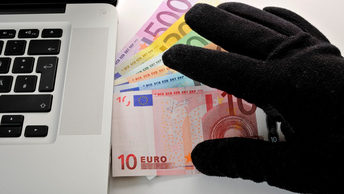 Laptop, PC, diverse EURO-Banknoten und eine Hand, die nach dem Geld greift (Symbolbild)