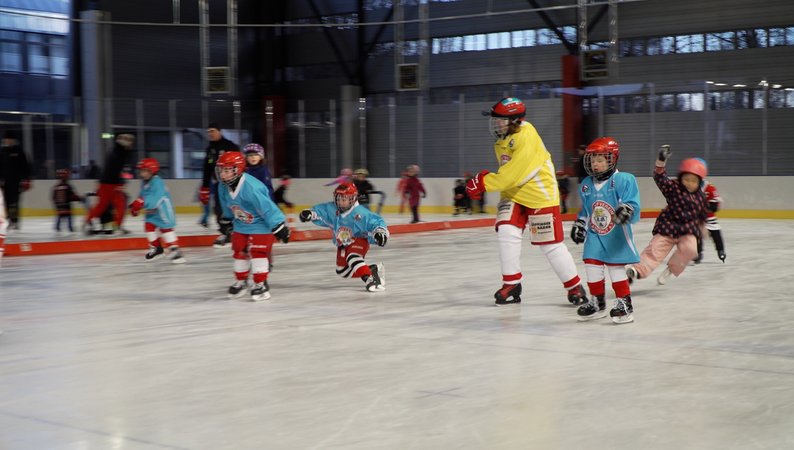 Kinder in Eishockeyausrüstung fahren Schlittschuh.