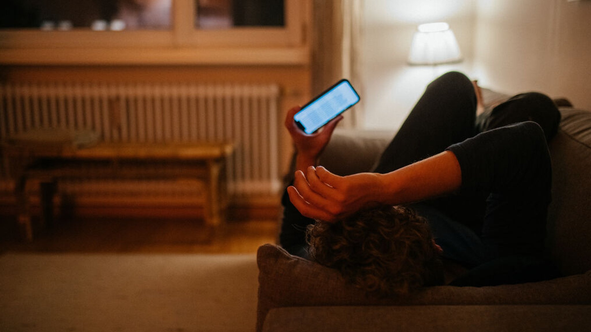 Ein junger Mann liegt auf dem Sofa und schaut in sein Handy.