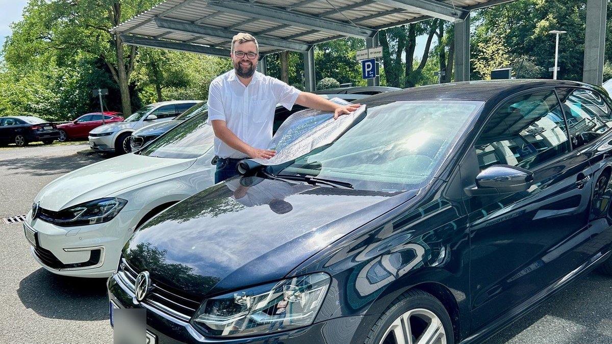 Ein Mann befestigt einen Thermo-Scheibenschutz auf der Windschutzscheibe eines Autos.