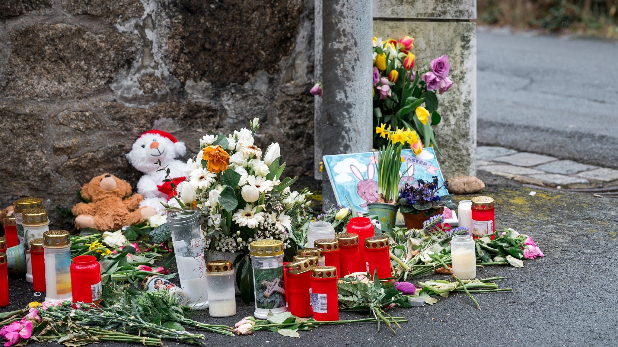 ARCHIV - 12.04.2023, Bayern, Wunsiedel: An einer Mauer vor dem Kinder- und Jugendhilfezentrum, in dem eine Zehnjährige tot aufgefunden wurde, liegen Blumen, Kuscheltiere und Kerzen. (zu dpa: «Tod in Kinderheim - Prozess gegen 25-Jährigen beginnt») Foto: Daniel Vogl/dpa +++ dpa-Bildfunk +++