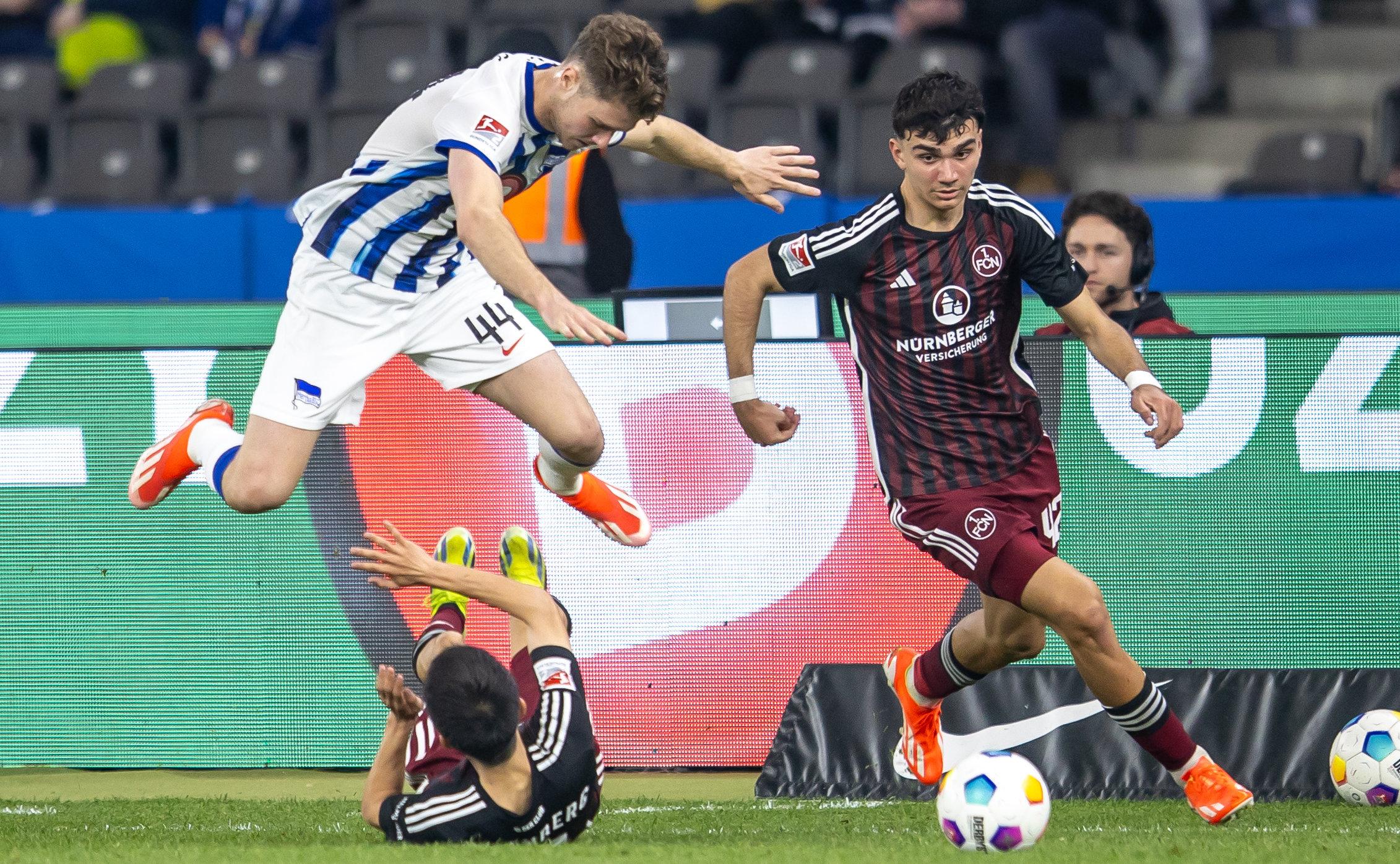 30.03.2024, Berlin: Fußball: 2. Bundesliga, Hertha BSC - 1. FC Nürnberg, 27. Spieltag, Olympiastadion. Berlins Linus Gechter (l-r) springt über Jens Castrop von 1. FC Nürnberg im Kampf gegen Can Uzun. 