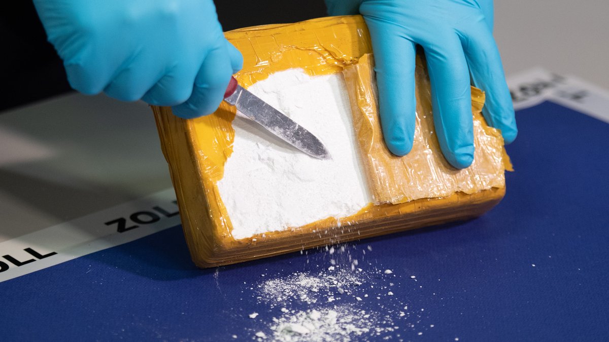 Symboldbild: Ein Polizist kratzt Kokain aus einem Paket. 