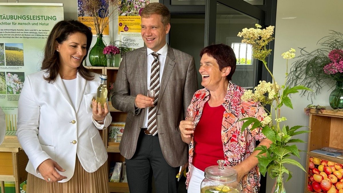 Bayerns Landwirtschaftsministerin Michaela Kaniber hält auf der Landesgartenschau eine Flasche selbstgemachten Saft in der Hand. Neben ihr der Bürgermeister und eine Frau.