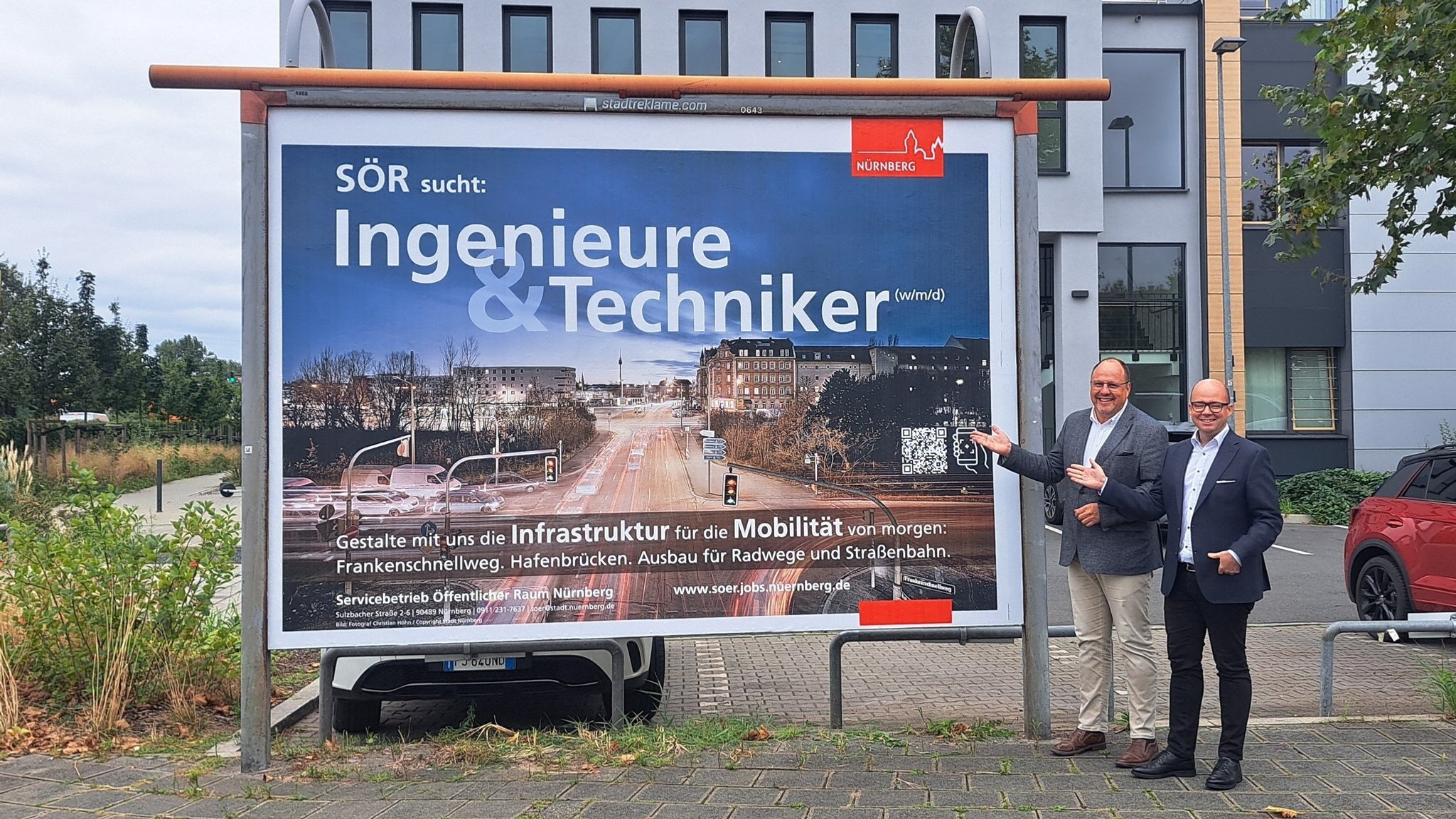 Bürgermeister Christian Vogel (SPD) und Personalreferent Thorsten Brehm (SPD) zeigen auf eine Plakatwand.