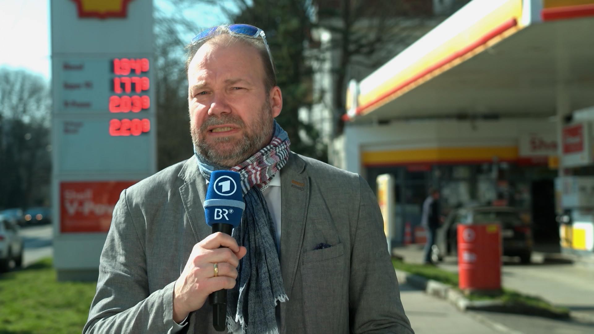 Ein Mann mit BR-Mikrofon vor einer Tankstelle.