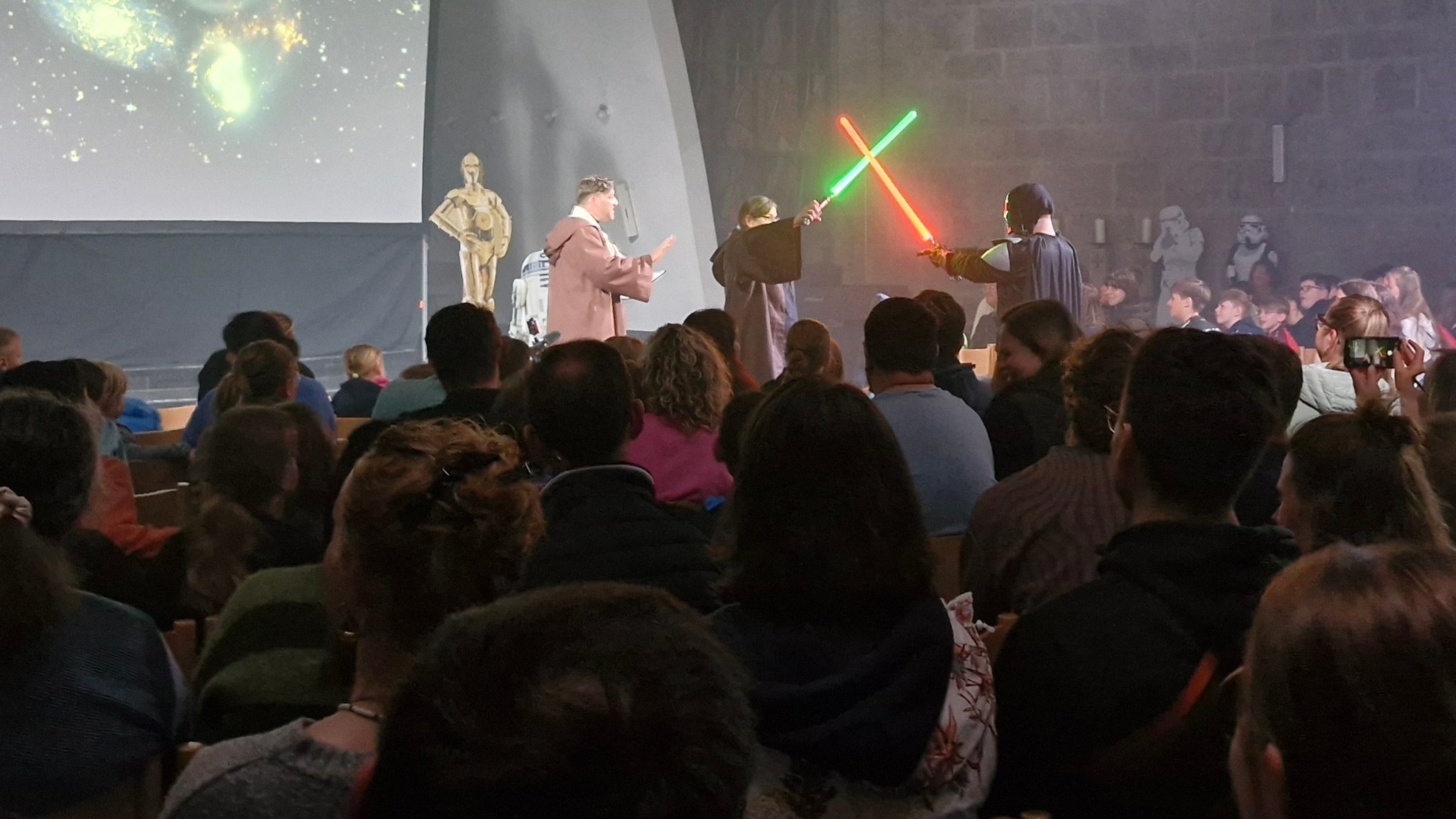 Mitten in der Kirche kämpfen  ein Jedi und Darth Vader mit einem roten und einem grünen Lichtschwert gegeneinander.