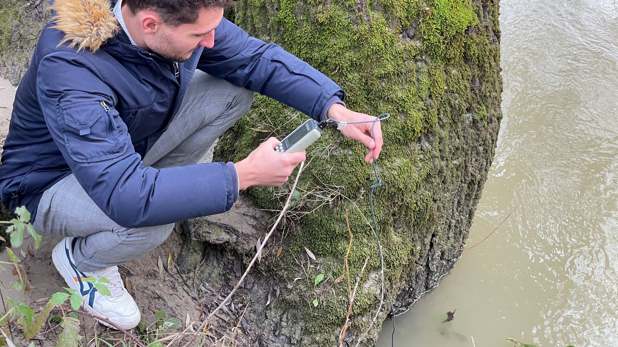 Bachelorant Valentin Pröpster hält ein Thermometer in die Donau bei Neuburg.