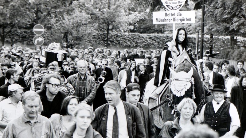 "Biergarten-Trauermarsch" zur Rettung der Bayerischen Biergartenkultur der Großhesseloher Waldwirtschaft in Pullach. Aufgrund eines Streits mit dortigen Nachbarn, sollte laut einem Gerichtsentscheid das Ausschenken von Bier nach 21.00 untersagt werden. Tausende Münchner demonstrierten im Jahr 1995 mit der "1. bayerischen Biergartenrevolution" schließlich erfolgreich dagegen. | Bild: picture alliance / SZ Photo | Claus Schunk "Biergarten-Trauermarsch" zur Rettung der Bayerischen Biergartenkultur der Großhesseloher Waldwirtschaft in Pullach. Aufgrund eines Streits mit dortigen Nachbarn, sollte laut einem Gerichtsentscheid das Ausschenken von Bier nach 21.00 untersagt werden. Tausende Münchner demonstrierten im Jahr 1995 mit der "1. bayerischen Biergartenrevolution" schließlich erfolgreich dagegen.