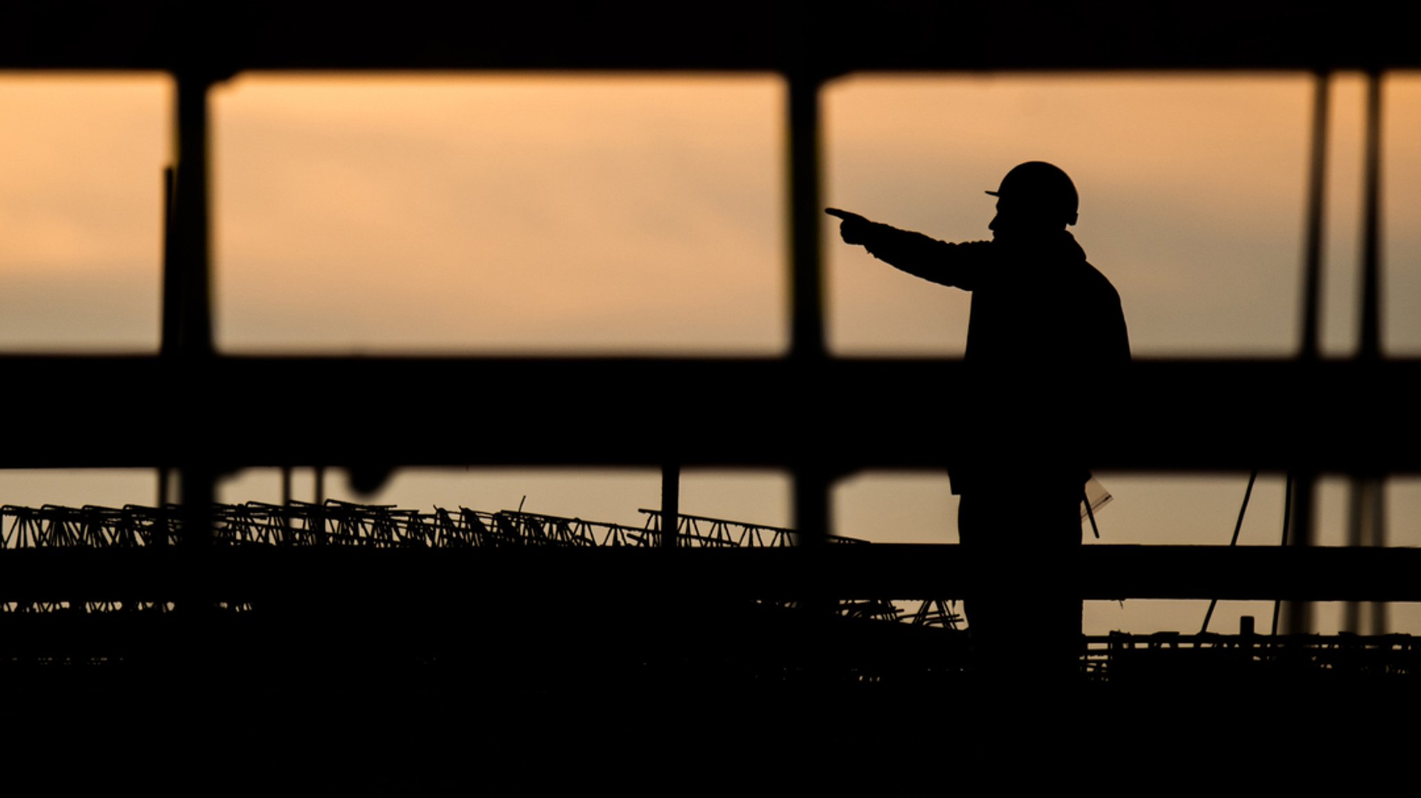 Die Silhouette eines Bauarbeiters zeichnet sich auf einer Baustelle vor dem verfärbten Morgenhimmel ab. | Bild: dpa-Bildfunk/Julian Stratenschulte Die Silhouette eines Bauarbeiters zeichnet sich auf einer Baustelle vor dem verfärbten Morgenhimmel ab.