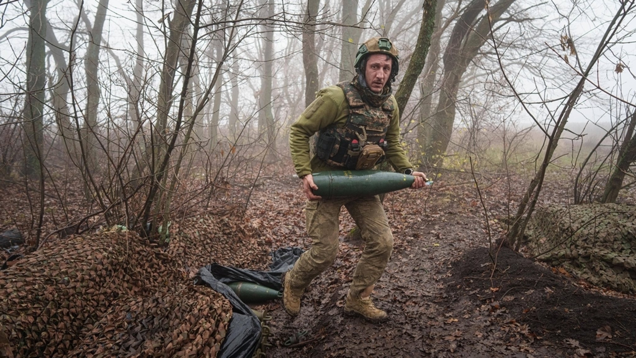 28.11.2025, Ukraine, Gebiet Pokrowsk: Ein ukrainischer Soldat des Bataillons Da Vinci Wolves trägt eine Artilleriegranate, bevor er auf russische Stellungen an der Frontlinie in der Ostukraine feuert.