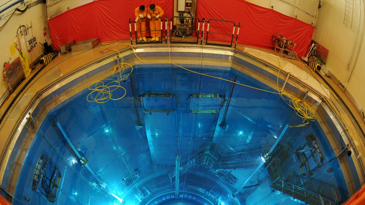 Archivbild: Zwei Mitarbeiter in orange-farbenen Anzügen blicken in den mit Wasser befüllten Reaktorbehälter von Isar 2.