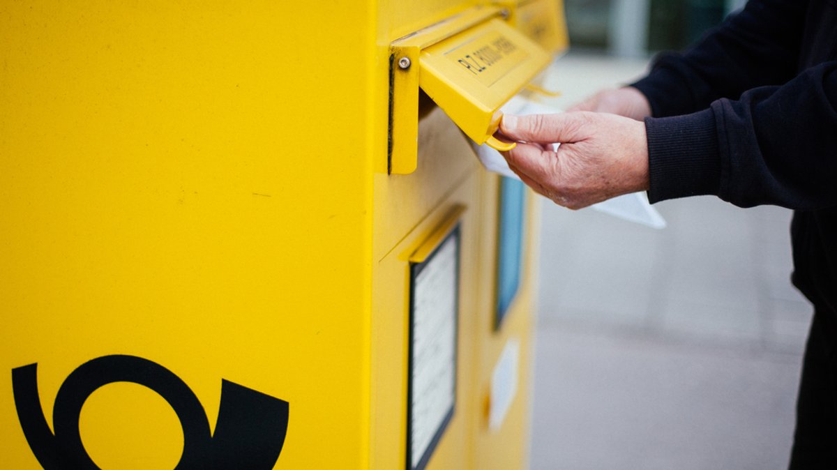 Ein Mann wirft einen Brief in einen Briefkasten der Deutschen Post in der Stadt.
