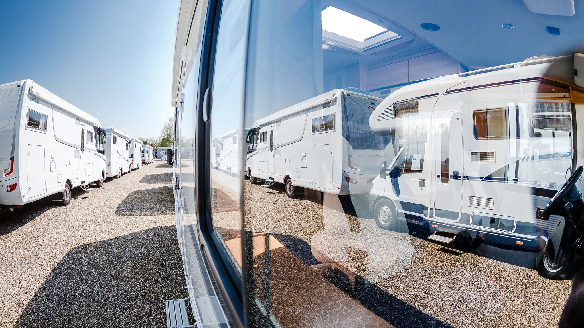 Gebrauchte Wohnmobile spiegeln sich im Fenster eines Wohnmobils. 