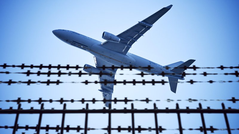 Symbolbild: Stacheldraht und Flugzeug | Bild: picture alliance / CHROMORANGE | Christian Ohde Symbolbild: Stacheldraht und Flugzeug