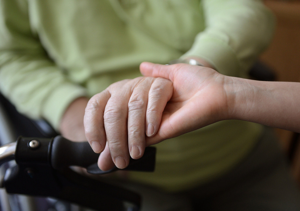 Die Hand einer Pflegekraft hält die Hand einer Pflegebedürftigen.