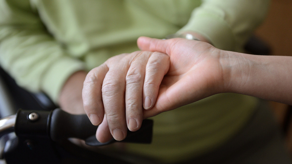 Die Hand einer Pflegekraft hält die Hand einer Pflegebedürftigen.